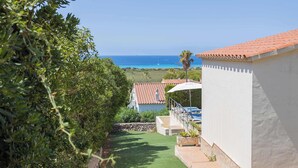 Une propriété située sur la côte, offrant une vue sur la mer, avec une terrasse agrémentée d’un parasol blanc et un jardin.
