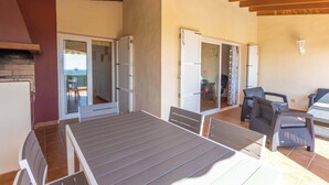 Un espace patio avec une table et des chaises, une porte-fenêtre coulissante donnant sur un balcon et une cheminée en briques.
