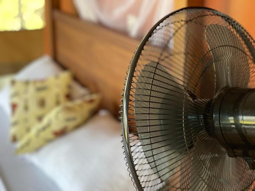 A close-up of a room with a bed, a yellow patterned blanket, and a wall-mounted fan.