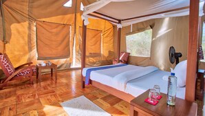 Una habitación con carpa, una cama, una silla, una mesa y un ventilador.