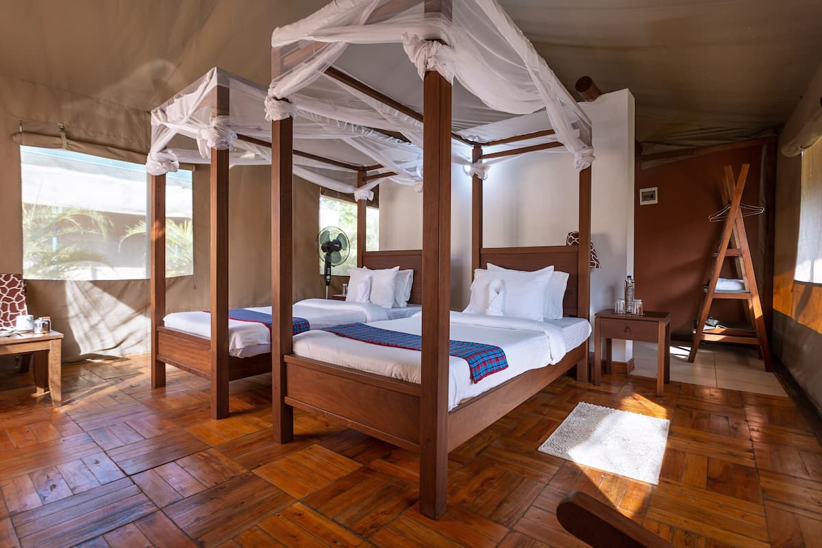 A four-poster bed with white linens, a wooden floor, and a fan in the corner.