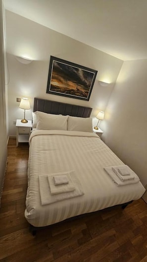 A neatly made bed with a striped bedspread and two folded towels, a dark headboard, and two bedside lamps on white nightstands.
