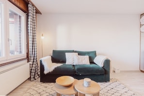 A cozy living room with a dark green sofa, two white pillows, a wooden bowl, and a patterned rug.