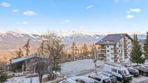 Un edificio a più piani con un'area di parcheggio antistante, circondato da montagne innevate e alberi.