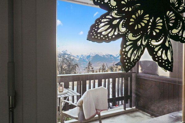 A balcony with a view of snow-capped mountains, a wooden railing, and a chair with a white cover.