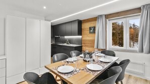 Een moderne eethoek met een houten tafel voor vier personen, een keuken met donkere kastjes en een raam met uitzicht op bomen.