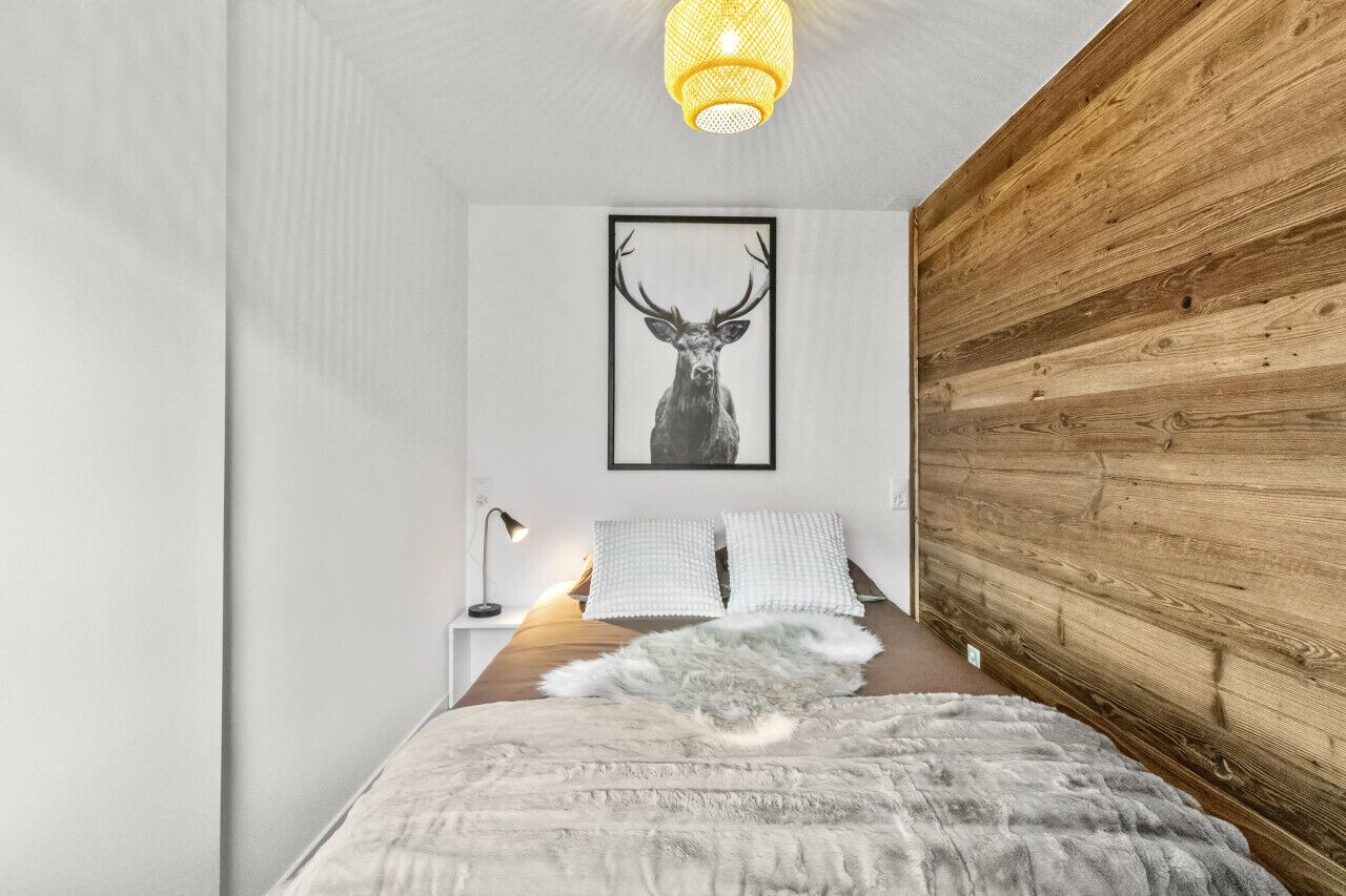 Une chambre à coucher avec une tête de lit en bois, un tableau représentant un cerf encadré, une couvre-lit blanche et une petite lampe de chevet.