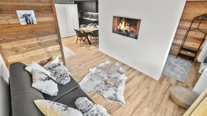 Een moderne woonkamer met een houten accentmuur, een open haard, een eethoek en een keuken op de achtergrond.