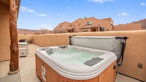A hot tub on a patio with a view of a mountain and a house in the background. - Rim Village X3 - Large Patio & Private Hot Tub (Moab)