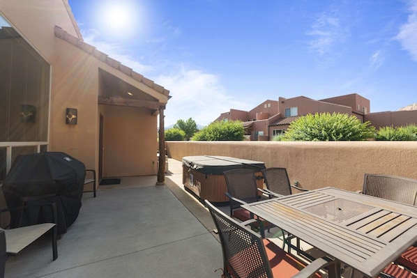 An outdoor patio area with a barbecue grill, a table with chairs, and a view of neighboring buildings. - Rim Village X3 - Large Patio & Private Hot Tub (Moab)