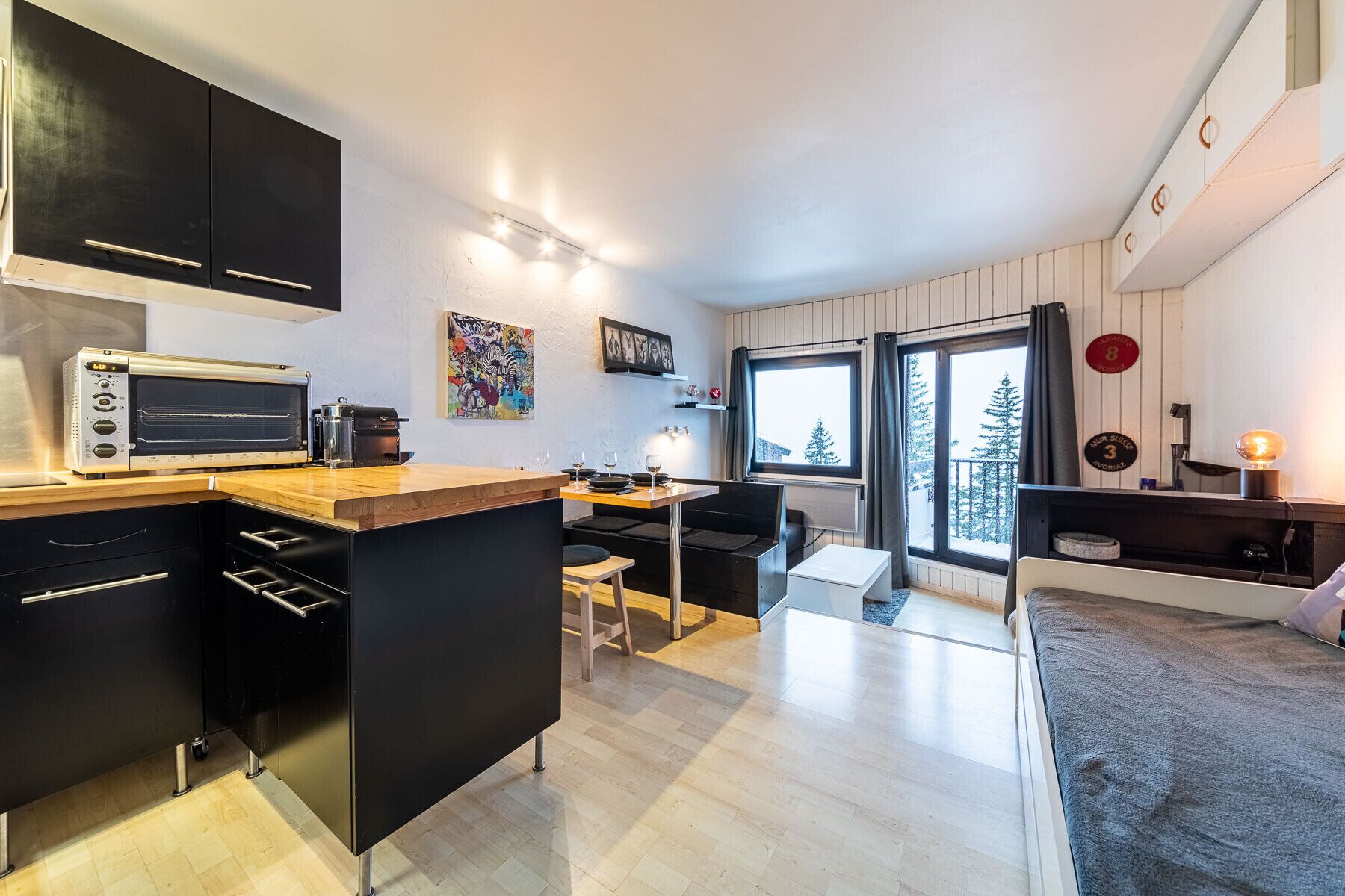 Een moderne keuken met een ingebouwde oven, een eethoek met tafel en stoelen, en een groot raam met uitzicht op bomen.