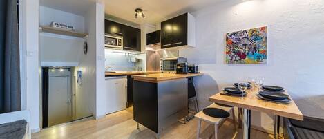 A compact kitchen with modern appliances, a dining area with a wooden table and chairs, and a colorful abstract painting on the wall.