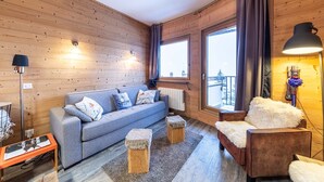 A cozy room with wooden walls, a grey sofa, a brown armchair, a small table, and a radiator. - Immodreams - Le Cocooning - Avoriaz (Avoriaz)