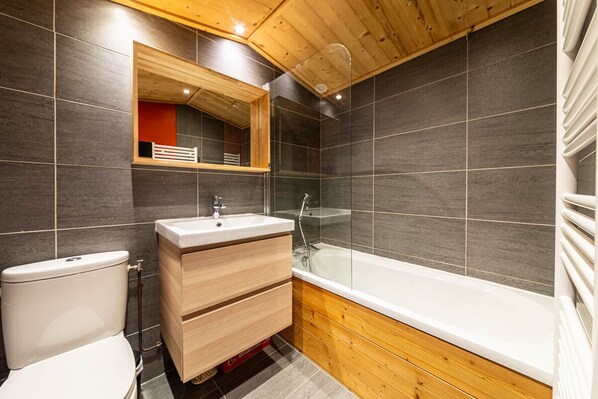 A modern bathroom with a wooden vanity, a toilet, and a bathtub.