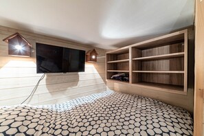 A room with a flat-screen TV mounted on the wall, wooden shelves, and a patterned floor.