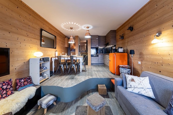 Un intérieur moderne avec des murs en bois, un coin repas, une cuisine et un salon comprenant un canapé et des poufs.