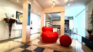 Un interno moderno con pavimento a scacchi, un divano rosso e una zona pranzo visibile attraverso un arco.