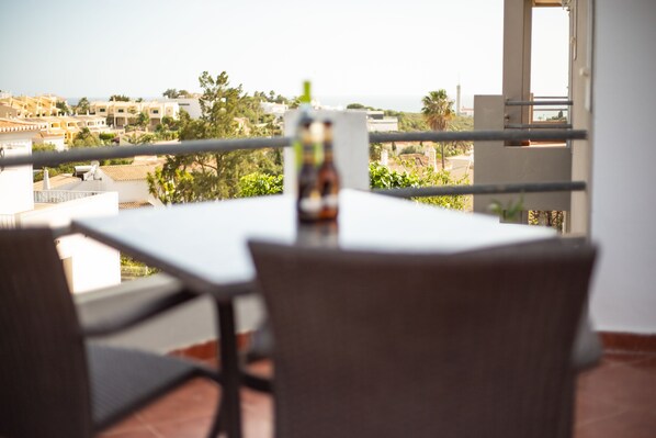 Ein Balkon mit Tisch und Stühlen, der auf eine Küstenstadt mit Gebäuden und Grünflächen blickt.