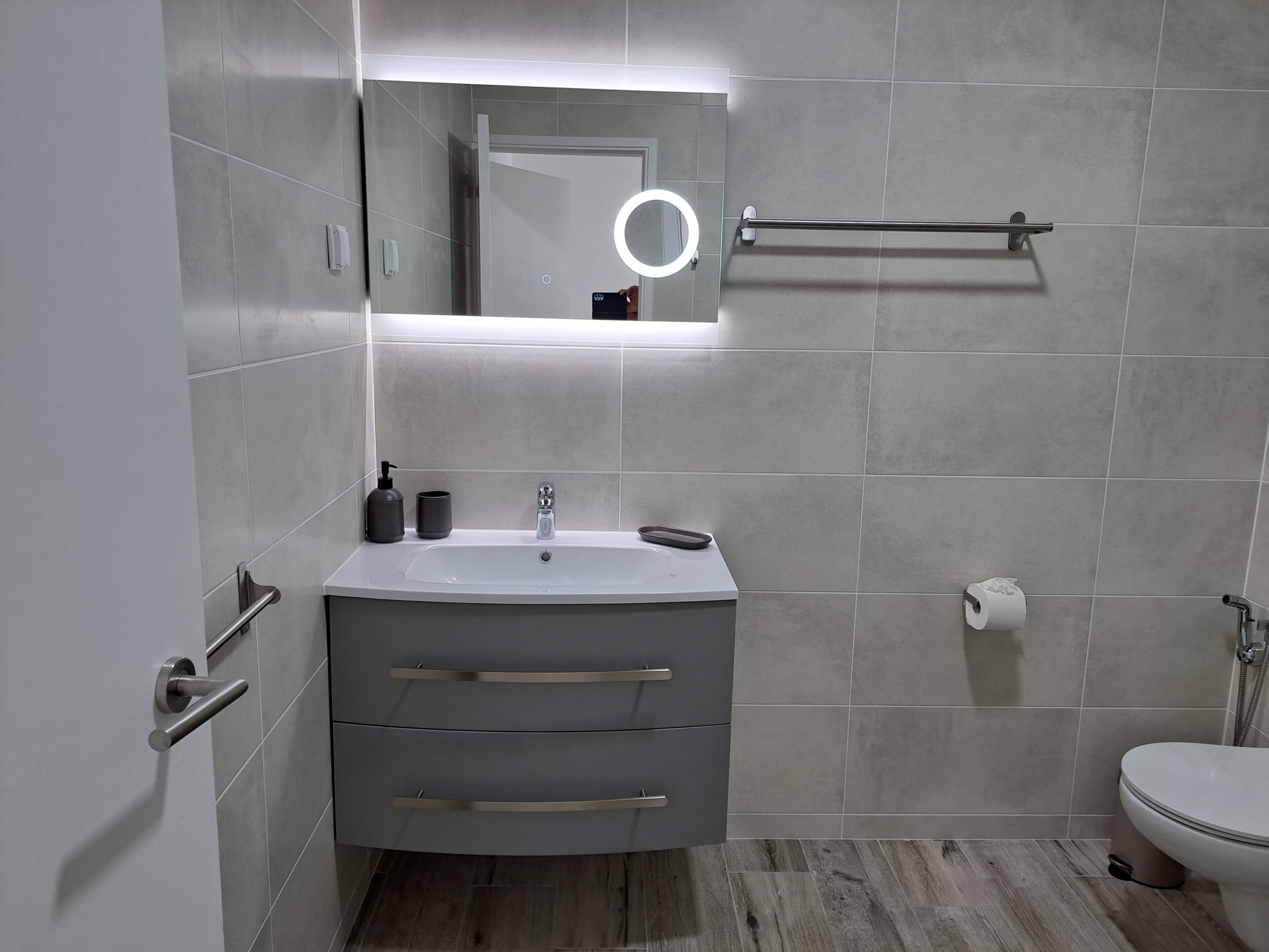 Ein modernes Badezimmer mit Waschbecken, Spiegel, Handtuchhalter, Toilette und Duschbereich.