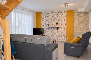 A living room with a grey sofa, a grey armchair, a television, and a floral wallpaper.