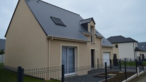 Una moderna casa a due piani con tetto spiovente, un piccolo garage adiacente e un cortile recintato.