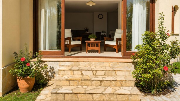 A house with a stone staircase leading to a glass door entrance, a wooden table with chairs, and potted plants. - Mediterranean Villa in Costa Brava with Pool, Garden, and Close to Beach (Calonge)