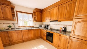 A kitchen with wooden cabinets, a microwave, and a dishwasher. - Mediterranean Villa in Costa Brava with Pool, Garden, and Close to Beach (Calonge)