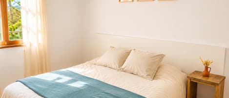 A bedroom with a bed, a bedside table with a vase, and three framed pictures on the wall.