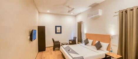 A hotel room with a bed, a desk, a chair, a TV, and an air conditioning unit.