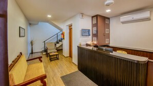 A reception area with a wooden bench, a reception desk, and a staircase leading to an upper floor. - Iyla Apart Hotel (Puducherry)