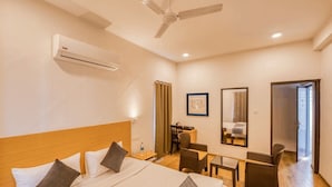 A hotel room with a bed, a desk, a chair, a ceiling fan, and an air conditioning unit. - Iyla Apart Hotel (Puducherry)