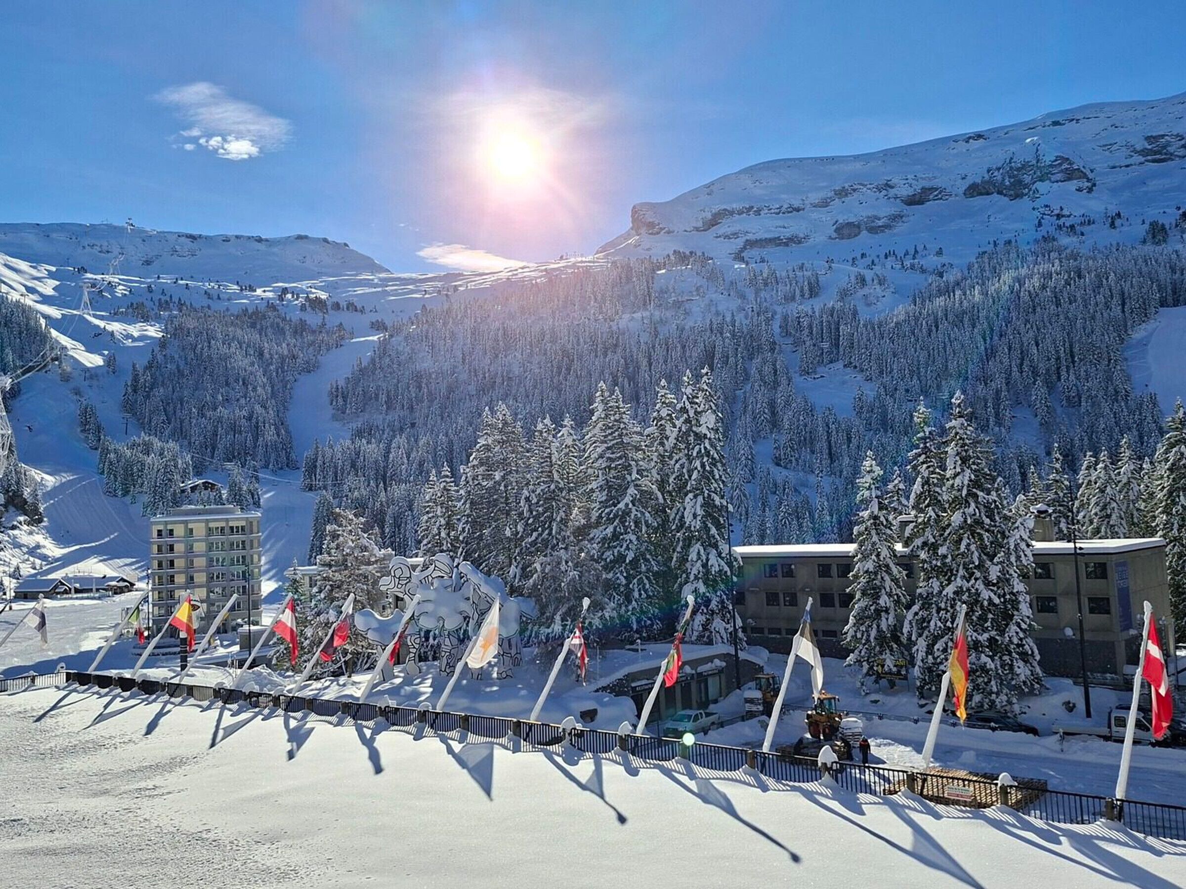 A snow-covered mountain landscape with a ski resort, buildings, and flags.