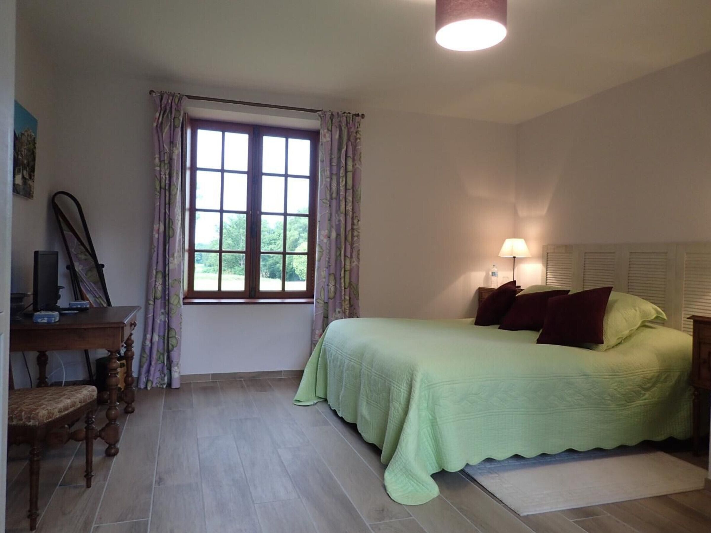 A bedroom with a bed, a desk, a chair, a window with curtains, and a lamp.