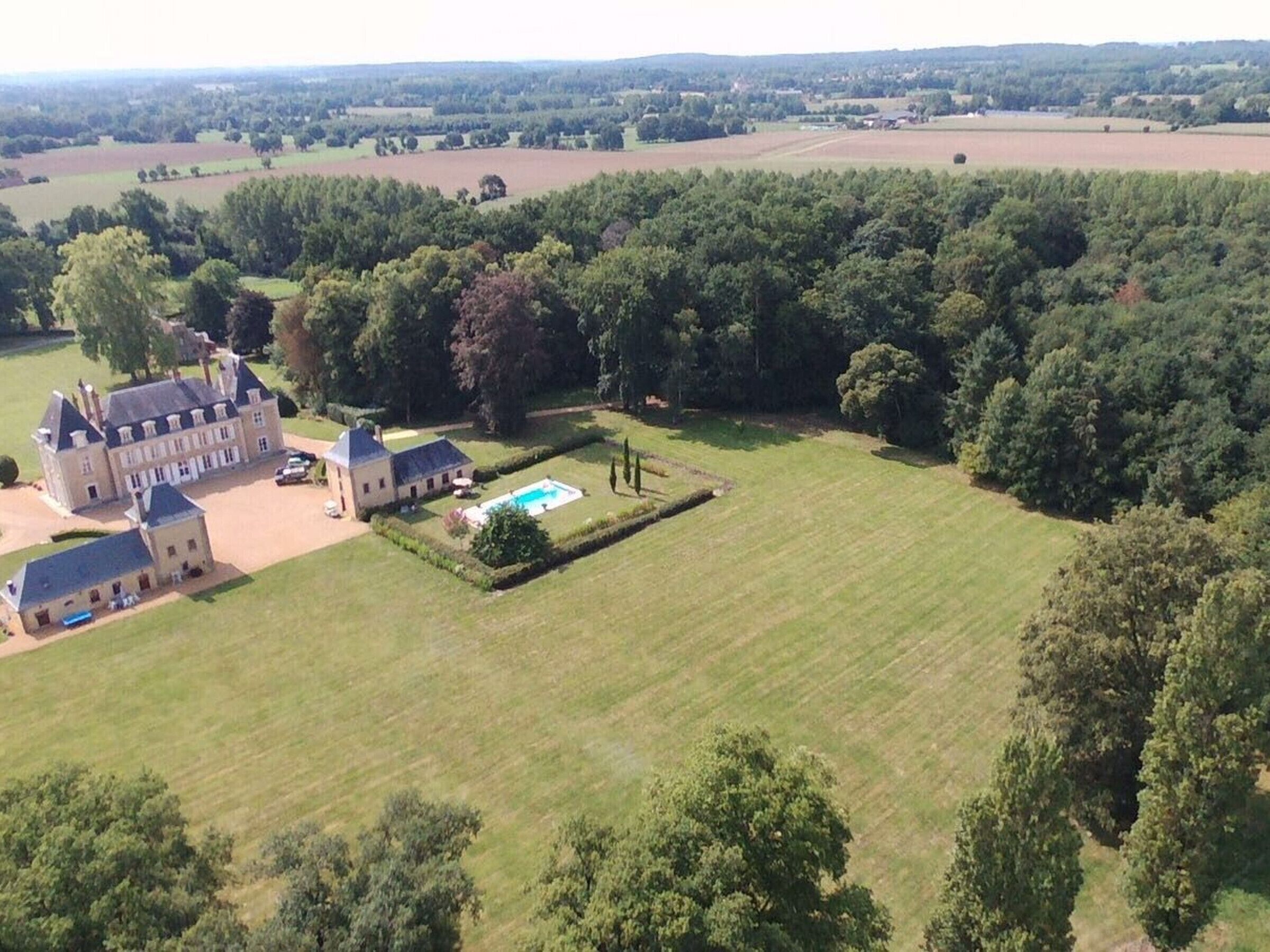 Vista aérea de una extensa propiedad con un edificio principal, una piscina y abundante vegetación circundante.