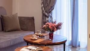 A cozy living room with a sofa, a round coffee table with a book, a vase with flowers, and a lamp. - Blue Ark Gate to History (Athens)