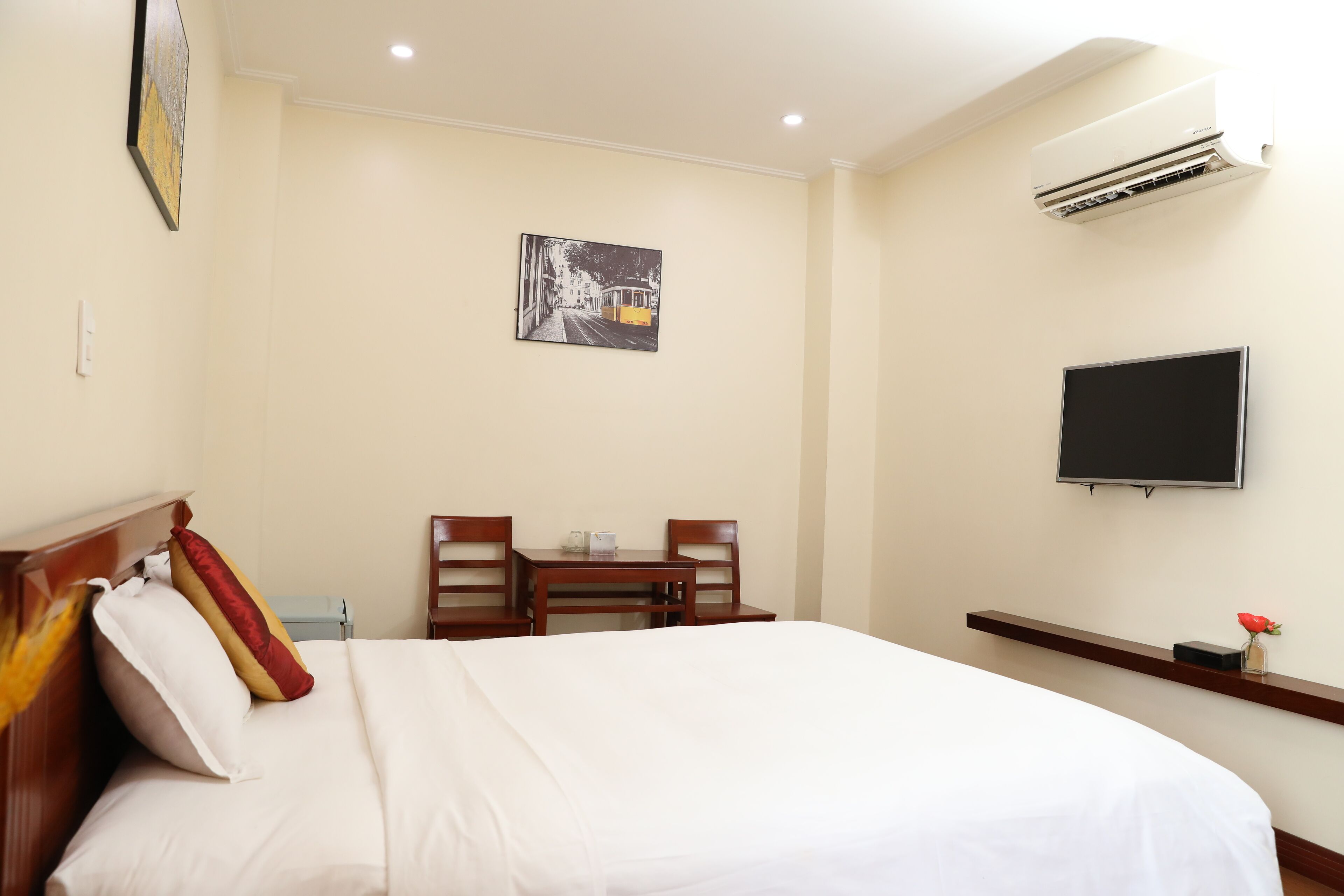 A hotel room with a bed, a desk with chairs, a flat-screen TV, and an air conditioning unit.