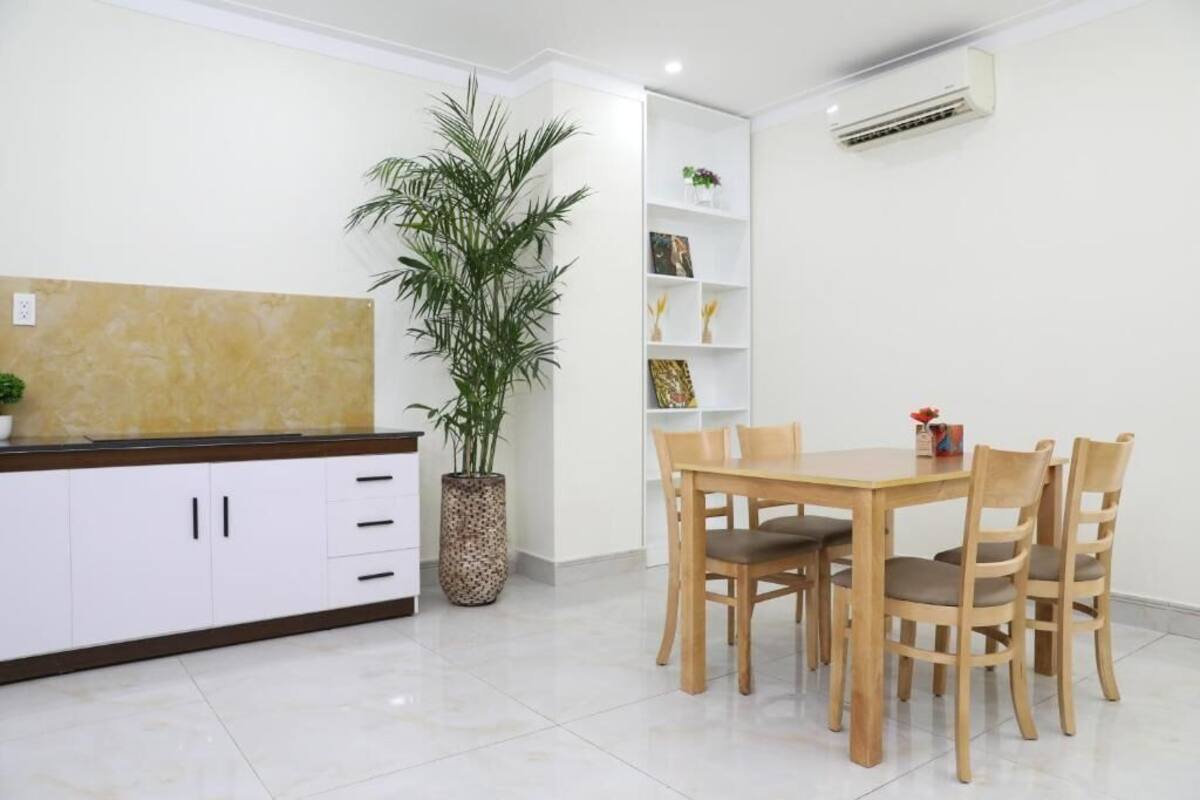 Une cuisine moderne avec des meubles blancs, une table à manger en bois et des chaises. On y trouve une plante en pot et une étagère avec des objets décoratifs.