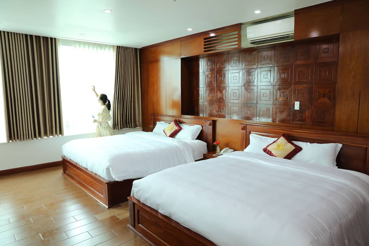 Une chambre d’hôtel avec deux lits, des têtes de lit en bois, une grande fenêtre avec des rideaux et un système de climatisation intégré.