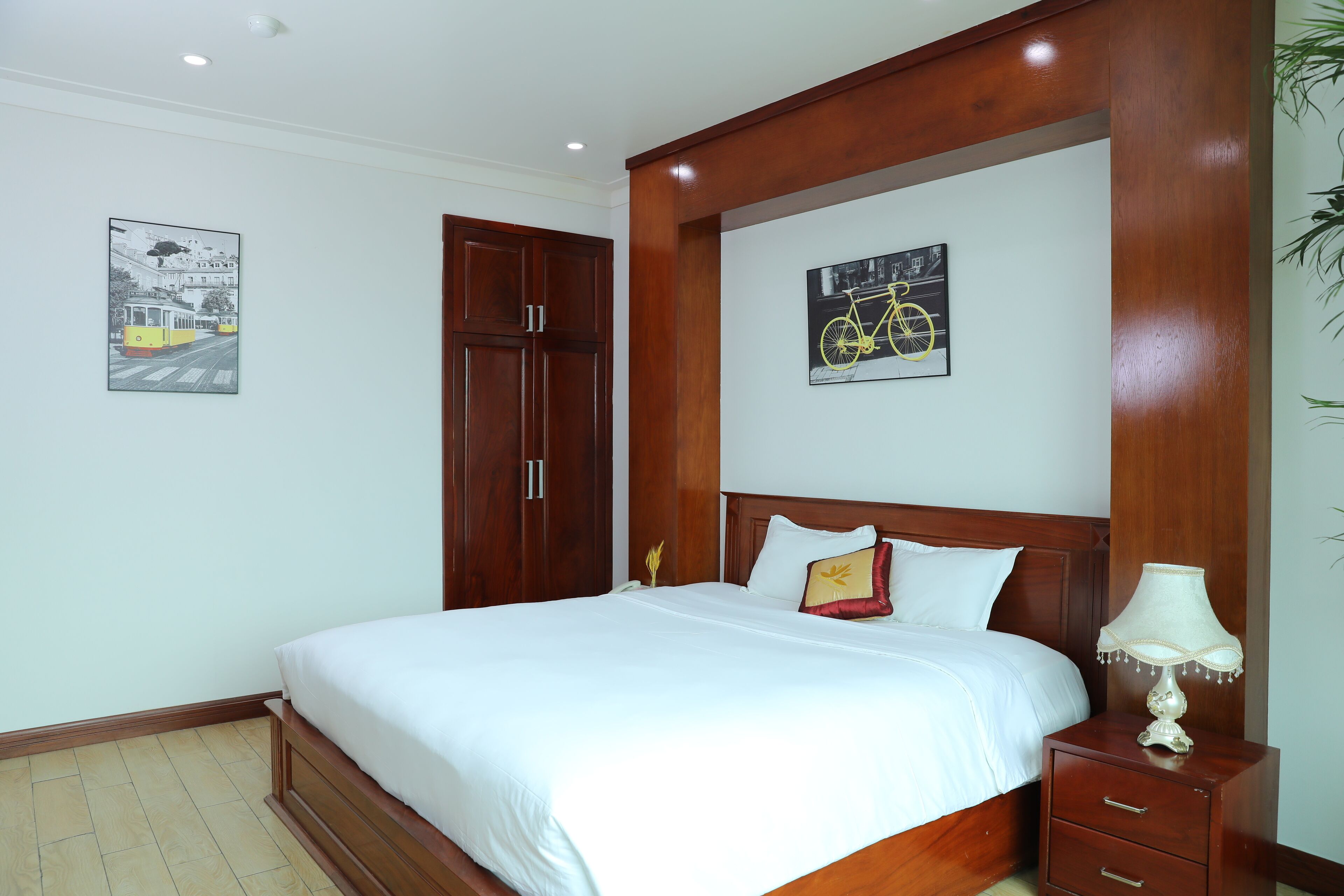 A neatly arranged bedroom with a large bed, wooden headboard, a nightstand with a lamp, and two framed pictures on the wall.