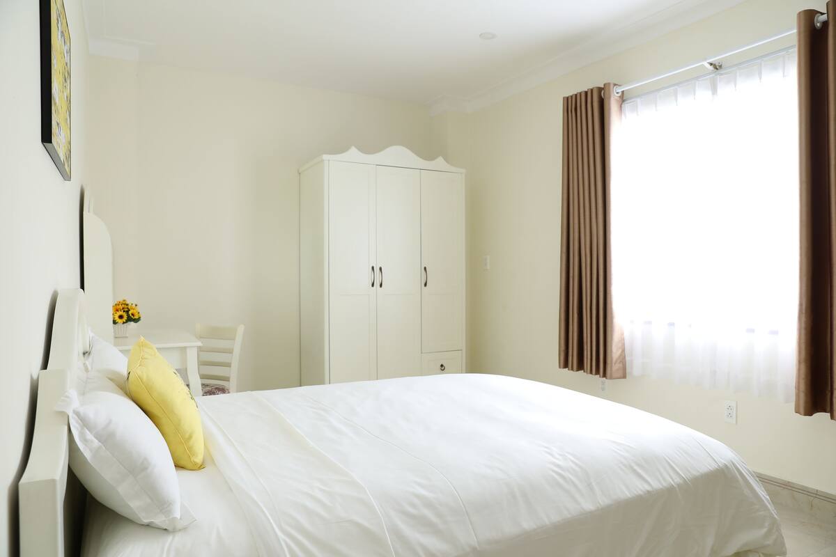 Une chambre à coucher avec un lit, une armoire blanche et une fenêtre avec des rideaux.