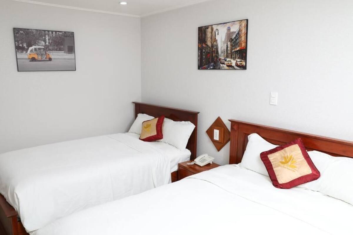 Une chambre d’hôtel avec deux lits, du linge de lit blanc, une tête de lit en bois, une table de chevet avec un téléphone et deux tableaux accrochés au mur.