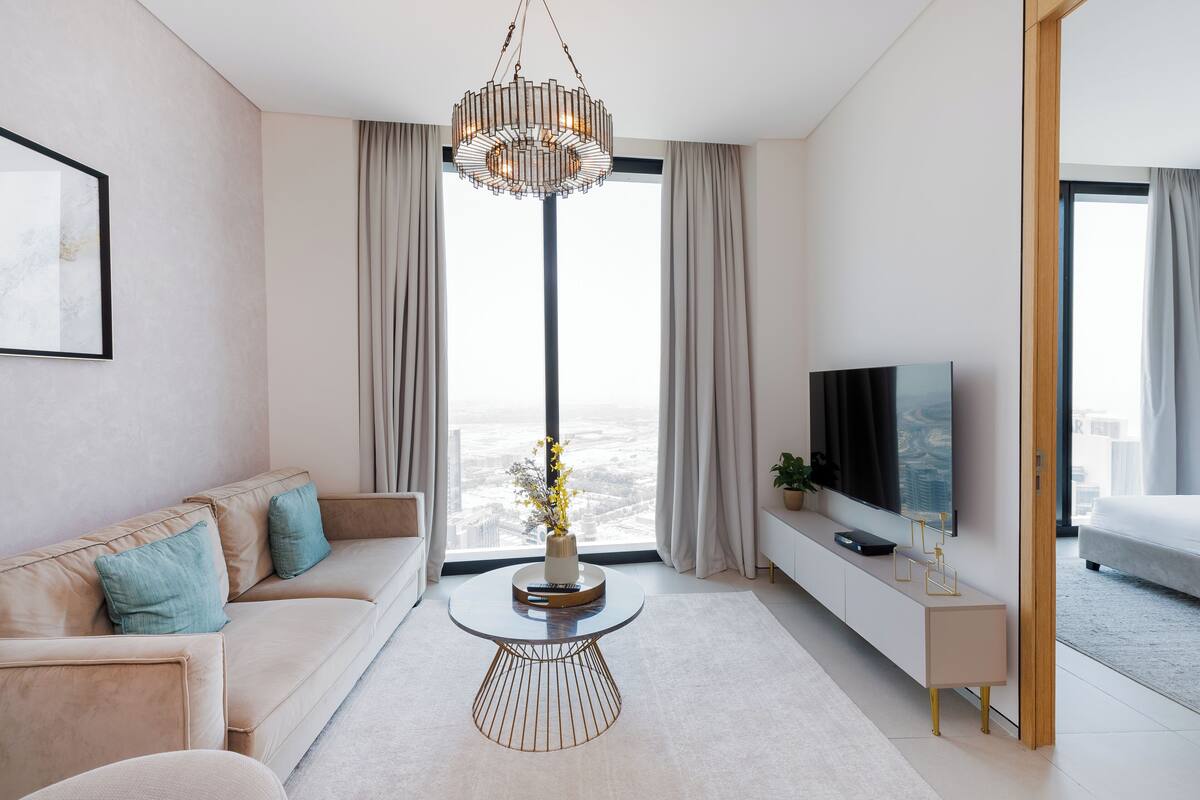 A modern living room with a sofa, a round coffee table, a TV, and a view of the city through large windows.