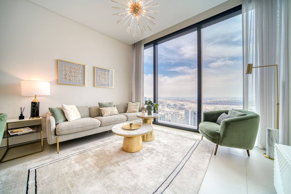 A modern living room with a large window, a sofa, a coffee table, and a green armchair.