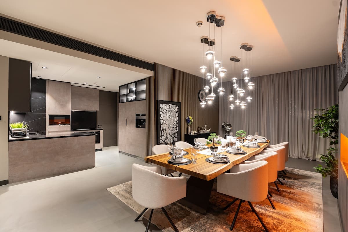 A modern dining area with a long wooden table, white chairs, and pendant lighting.