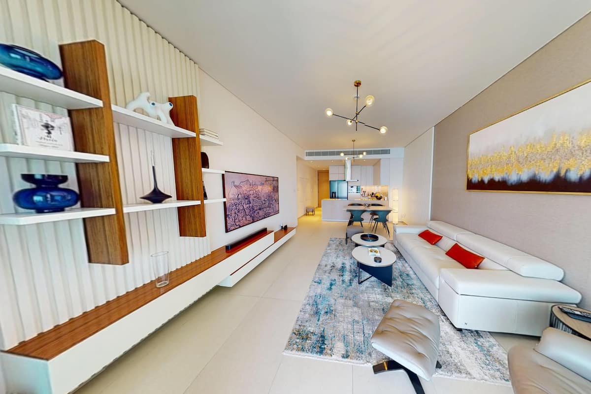 A modern living room with a white sofa, a coffee table, and a TV on a wooden shelf. There is a painting on the wall and a rug on the floor.