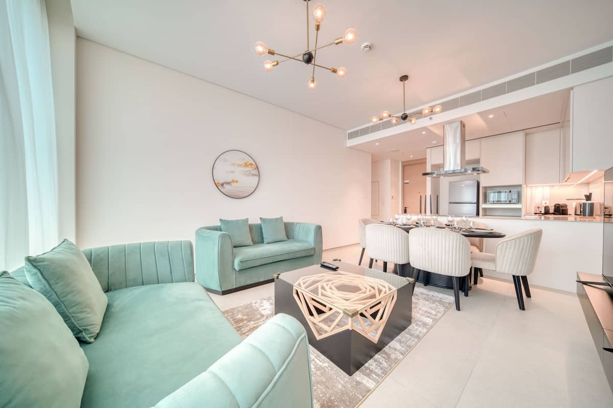 A modern living room with a teal sofa, a coffee table, and a dining area with white chairs.
