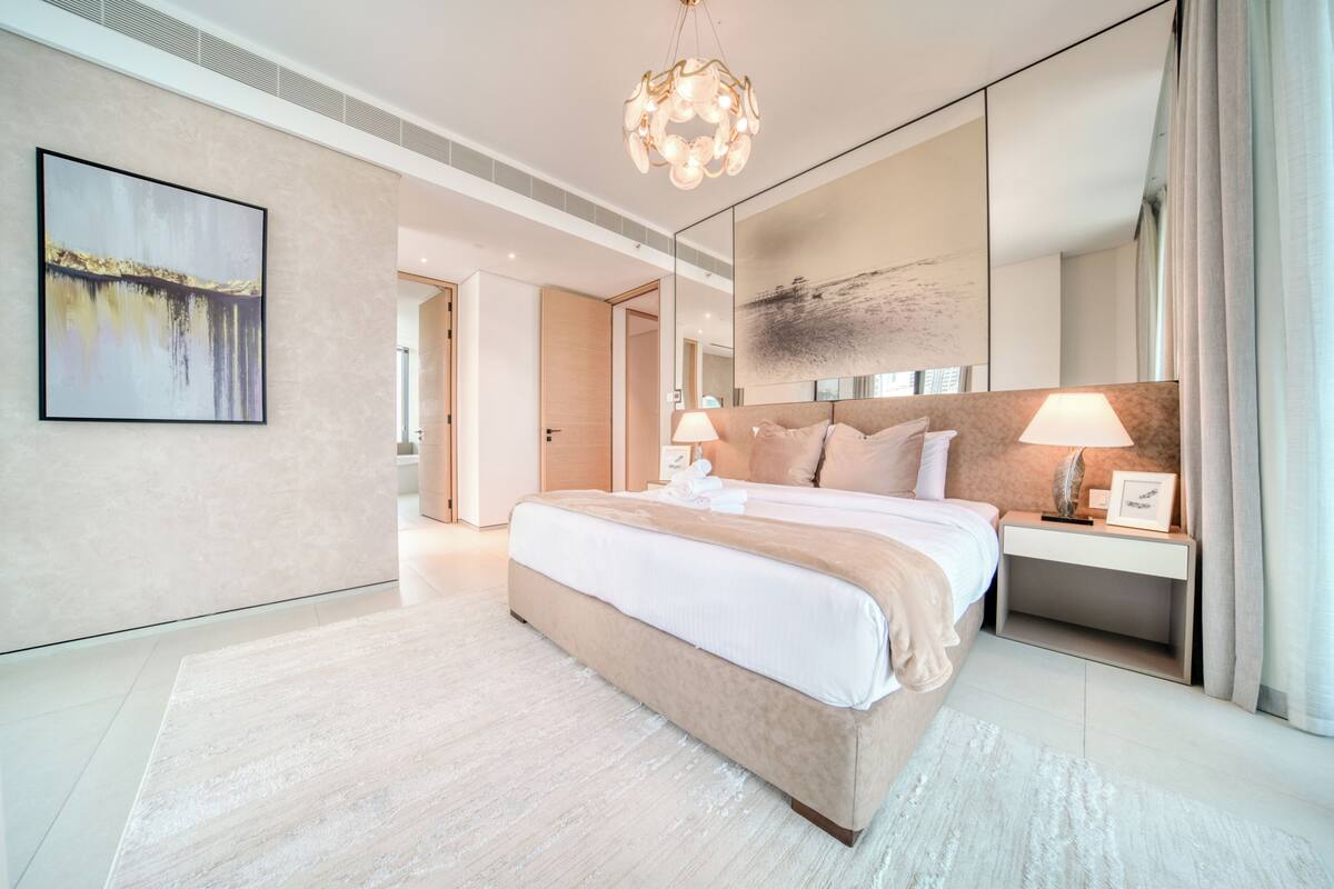 A modern hotel room with a large bed, bedside lamps, a nightstand, and a large mirror.