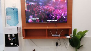 A television mounted on a wooden wall with a remote control on a wooden table in front. - Amazon one bedroom apartment  (Nakuru)