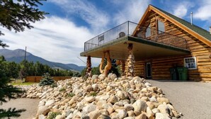 Una cabaña de troncos con balcón, rodeada por un muro de piedra y una valla de madera.