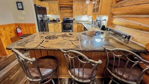 Una cocina con armarios de madera, una isla central con taburetes y electrodomésticos de acero inoxidable.